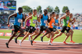 Athletes running on a track with a clear sky and stadium background